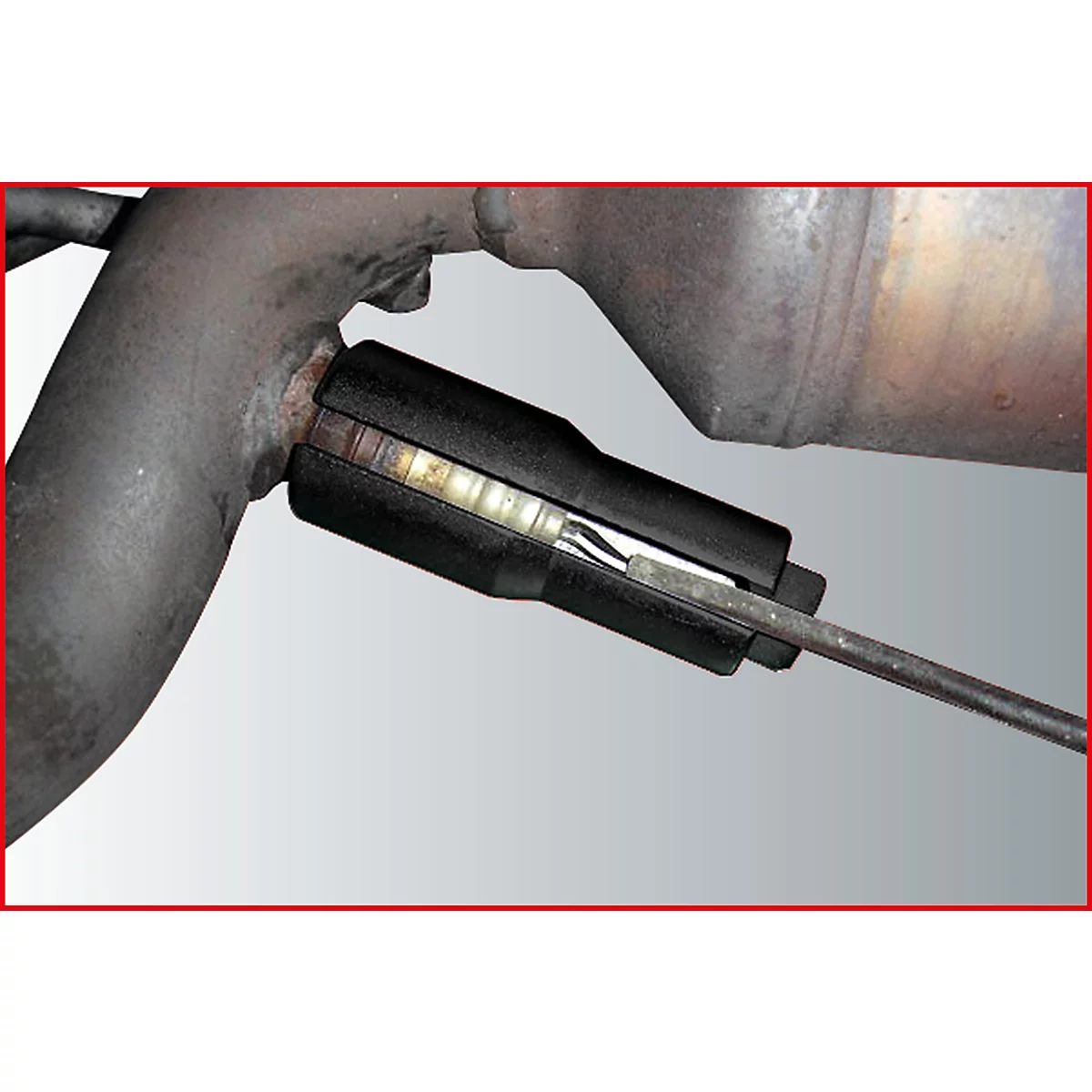 Nahaufnahme eines schwarzen Werkzeugs, das in einen Auspuff eingebaut ist. Es sind metallische Rohre und Bauteile zu sehen.